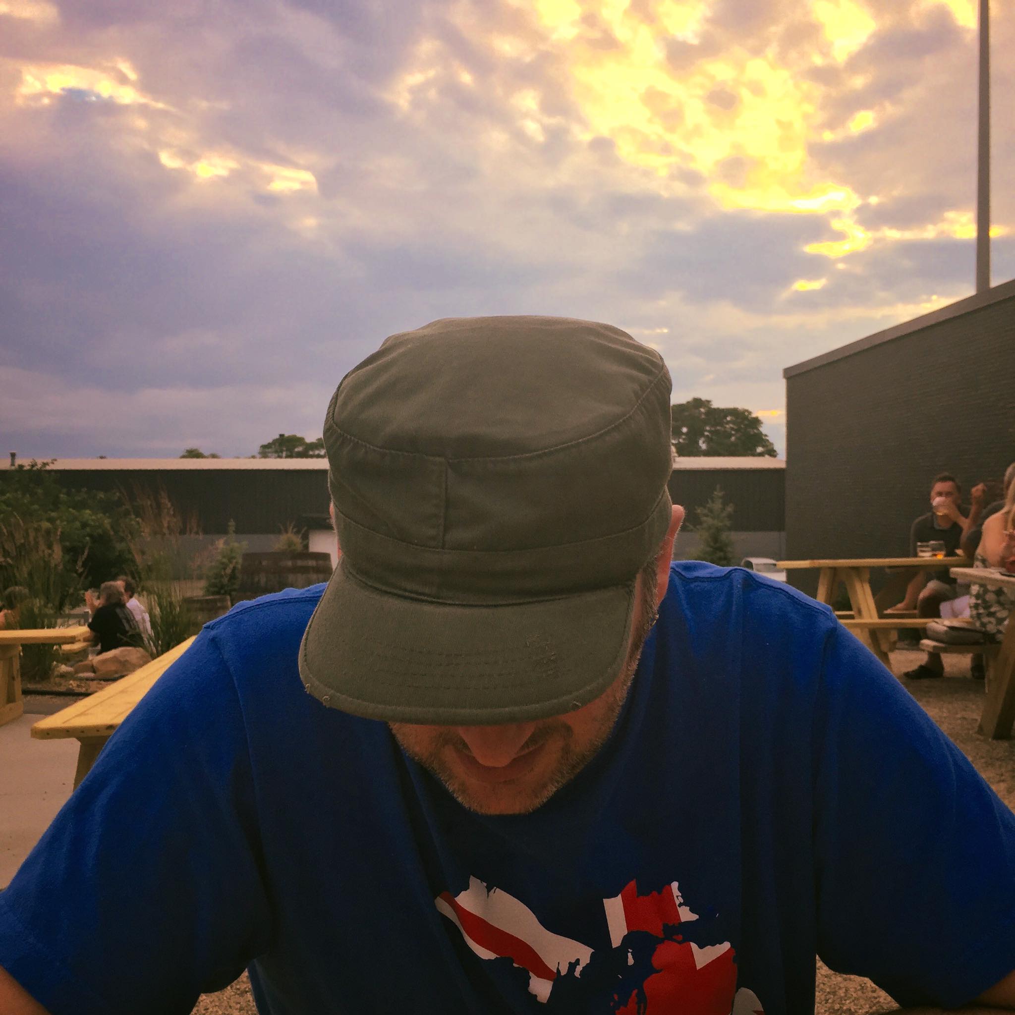 Mysterious, but probably incredibly handsome individual looks down with a cap covering their face. Behind them, a perfectly good sunset pales into insignificance.